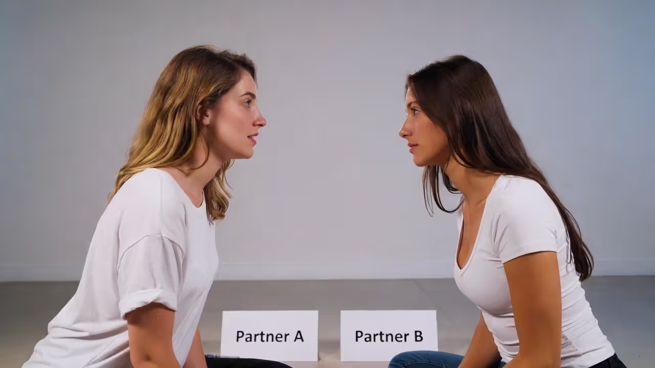 Two partners seated facing each other during a white tantric meditation, maintaining eye contact.